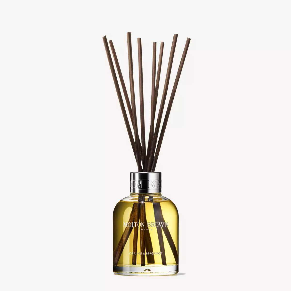 A clear glass bottle filled with yellow liquid, labeled &quot;MOLTON BROWN - ORANGE AND BERGAMOT DIFFUSER,&quot; features several long, thin, dark brown diffuser reeds extending from its neck. The reed diffuser boasts a hint of Sevillian orange and neroli. A metallic ring at its opening gives it an elegant and classy appearance.