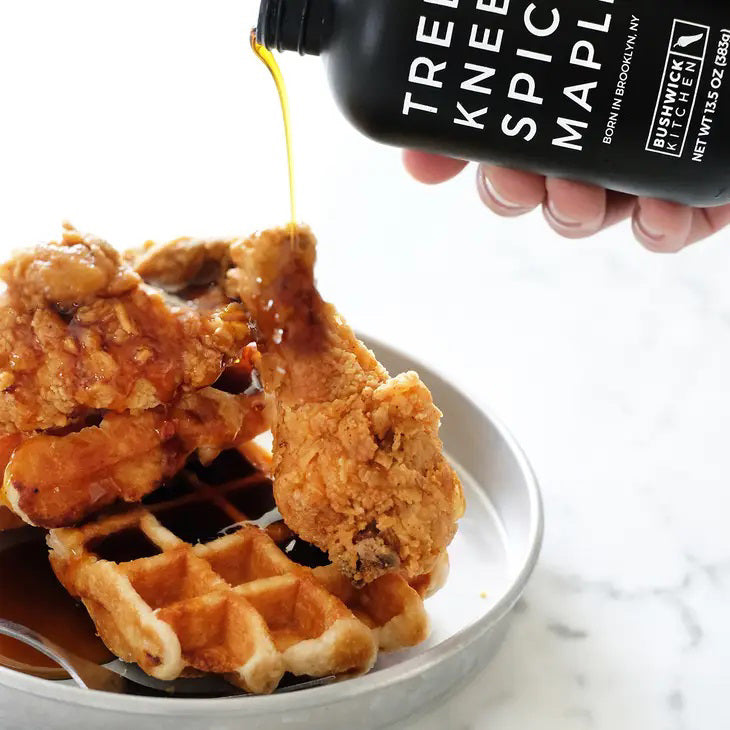 A black bottle with minimalistic design and white text that reads &quot;TREES KNEES SPICY MAPLE, BORN IN BROOKLYN, NY.&quot; Below the text is the &quot;BUSHWICK KITCHEN&quot; logo, along with &quot;NET WT 12.5 OZ (354g).&quot; The bottle features a screw cap. This BUSHWICK KITCHEN - &#39;TREES KNEES&#39; Spicy Maple Syrup is infused with habanero for the perfect kick.