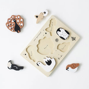 The WEE GALLERY - BIRDS TRAY PUZZLE is a wooden board featuring six bird-shaped pieces, including a toucan, peacock, penguin, swan, sparrow, and a small bird on a branch. This educational puzzle offers fun with its simple colors and shapes. The board is labeled with "wee gallery" and "Birds".