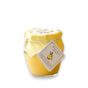 A jar of BELLA CUCINA - MEYER LEMON SPREAD adorned with bright yellow wrapping and a small tag tied around the top with string. The tag features an illustration of a lemon along with the text "Meyer Lemon spread." The jar is displayed on a reflective surface against a light background, making it perfect for enhancing any sweet tart or dessert.