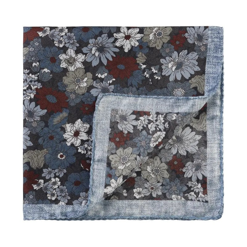 The AMANDA CHRISTENSEN Silk Pocket Square with Floral Pattern in Sky Blue Melange is an elegant men’s accessory featuring a square silhouette adorned with blue, gray, white, and burgundy flowers and finished with a light blue border. One corner is folded to showcase the reverse side of the luxurious silk fabric.