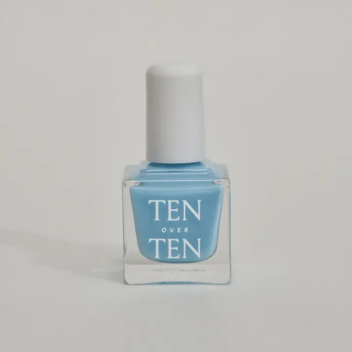 A glass bottle of TENOVERTEN - NAIL POLISH from the brand TEN OVER TEN, featuring a white cap and a dusty pink nail color. The front label displays "TEN OVER TEN" in white uppercase letters. This vegan, eight-free formula ensures both beauty and peace of mind. The background is plain and light-colored.