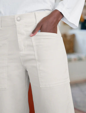 A person wearing FRANK & EILEEN’s Bray Everyday Barrel Pant in Italian Peached Twill Chalk pairs them with a white long-sleeve top, standing casually with one hand in their pocket.