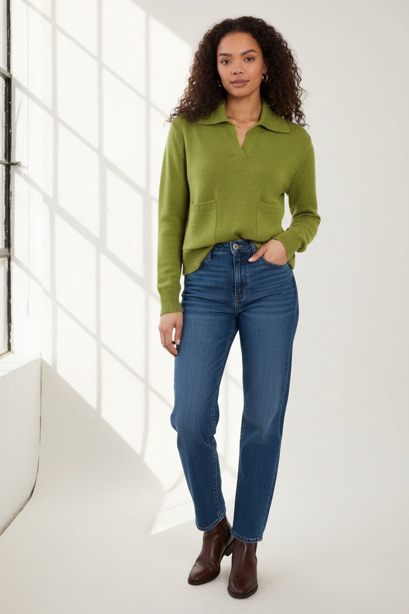A woman with curly hair wears the &amp; ISLA - Splitneck Pocket Polo in Moss by &amp; ISLA, paired with blue jeans, standing against a plain white background.