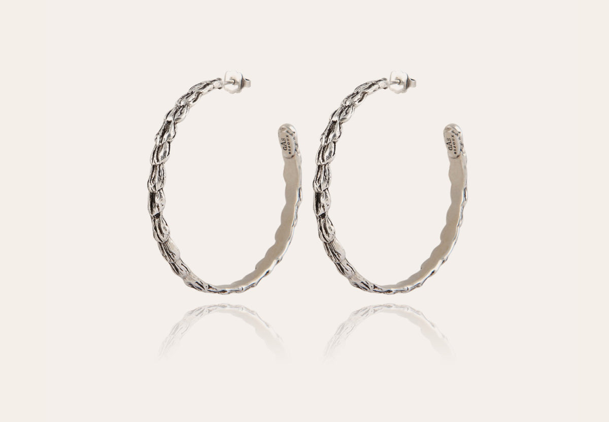 Introducing the GAS BIJOUX - LIANE SILVER HOOP EARRINGS: a stunning pair of 4.5 cm diameter, silver-plated earrings showcasing a twisted rope design set against a light background. These elegant hoops reflect subtle sophistication beneath them.