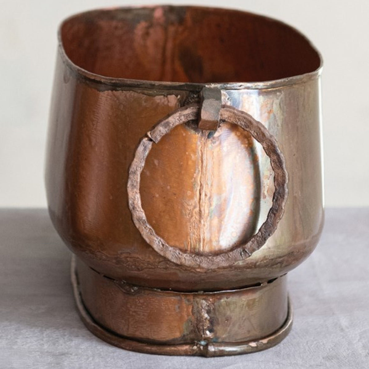 The OVAL METAL PLANTER WITH RING HANDLES, SMALL by CREATIVE COOP features a vintage oval design with ring handles and a charming, aged copper finish—an ideal accent for farmhouse decor.