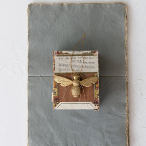 BEE ORNAMENT WITH WIRE LEGS by CREATIVE COOP, a gold resin bee hanging from a thin string with textured wings and thin wire legs in a polished gold finish.