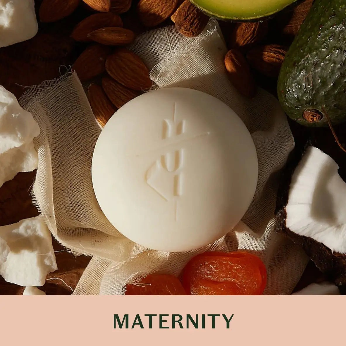 A green box labeled "KATE MCLEOD - MAMA STONE MINI DEEP MOISTURIZING LOTION BAR 1OZ" sits beside a round, white lotion bar partially wrapped in beige cloth—ideal for stretch mark prevention—on a peach background.