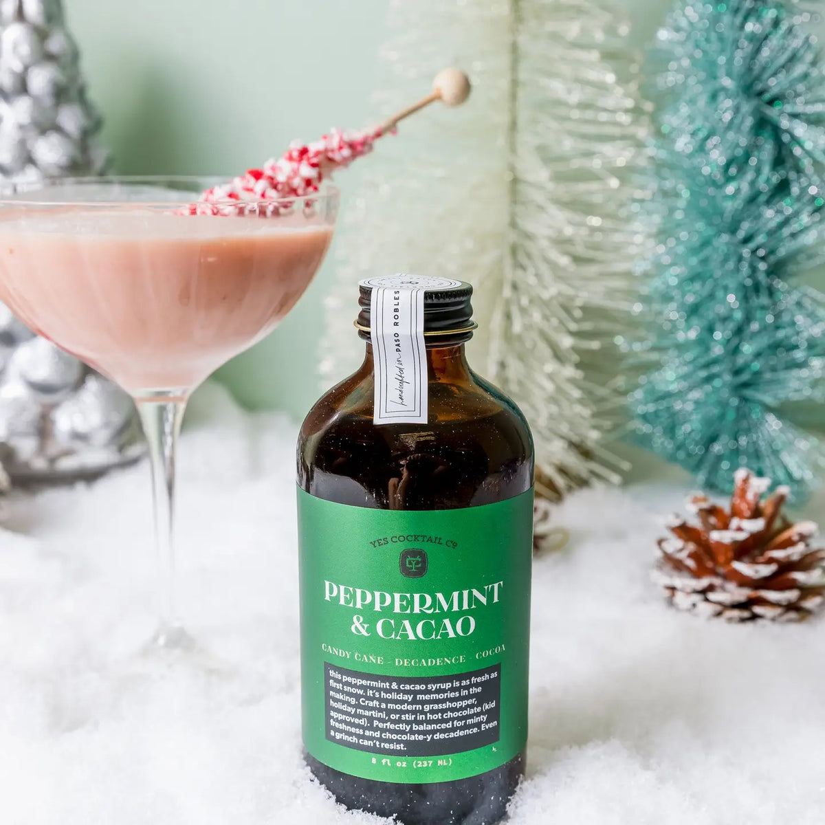 An 8 fl oz brown glass bottle from YES COCKTAIL CO. with a black cap, featuring a green label that reads “PEPPERMINT &amp; CACAO” in white text. The YES COCKTAIL CO. PEPPERMINT &amp; CACAO COCKTAIL SYRUP is an all-natural mixer blending candy cane freshness with decadent cocoa for a festive flavor experience.