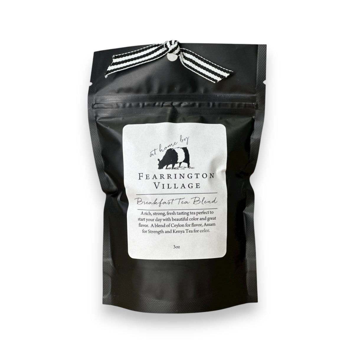 A black resealable bag of the Fearrington Signature Collection - Fearrington Signature Breakfast Tea Blend. The white label prominently displays the Fearrington House brand and describes it as &quot;An elegant blend of Ceylon and Assam with a hint of Keemun for strength.&quot; This loose leaf tea is adorned with a striped ribbon on top, offering a rich, strong tea experience.
