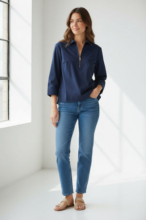 A woman with long dark hair models the HINSON WU Alessa 3/4 Sleeve Shirt in Stretch Polished Cotton Navy, featuring a collared neckline and gold zipper detail, paired with blue jeans against a plain beige background.