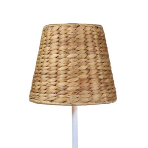 A modern poolside area features white lounge chairs, a potted fern, EMPIRE Water Hyacinth Woven Wicker Shade XXL by Zafferano America, white swan float, and a cordless lamp with glass water bottle on the table.