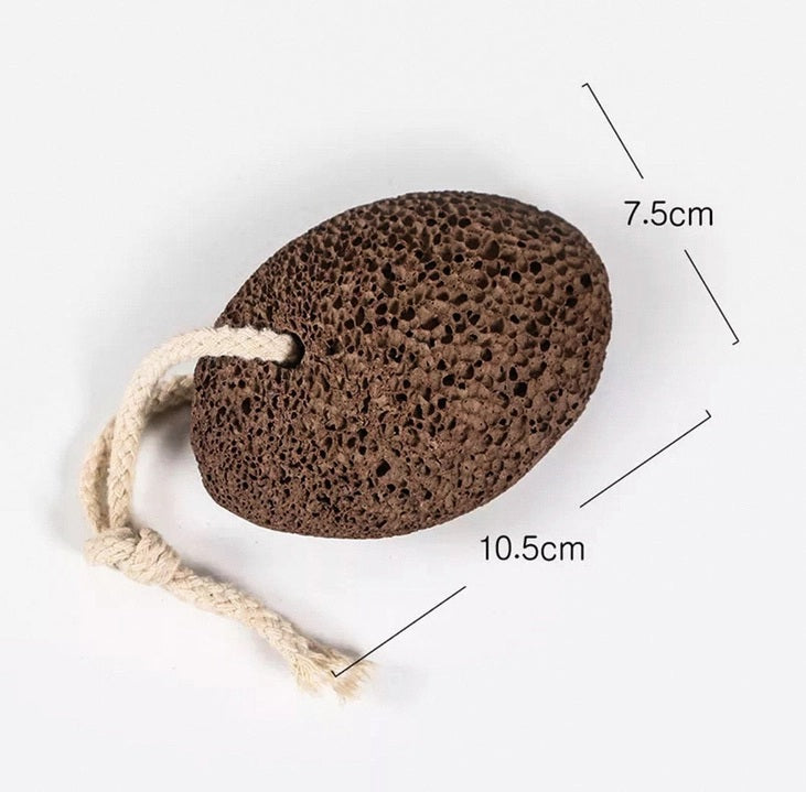 The SMILE BOUTIQUES NATURAL PUMICE STONE FOOT SCRUBBER features a brown, rough, and porous surface ideal for foot care and effective callus removal. It comes with a white rope loop for convenient hanging, as shown against a white background.