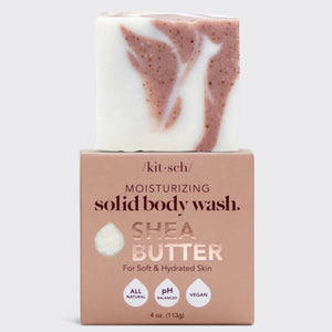 A bar of KITSCH - MOISTURIZING SHEA BUTTER BODY WASH with pink and white swirls rests on a pink box; this all-natural, pH balanced, vegan body wash leaves skin soft and hydrated.