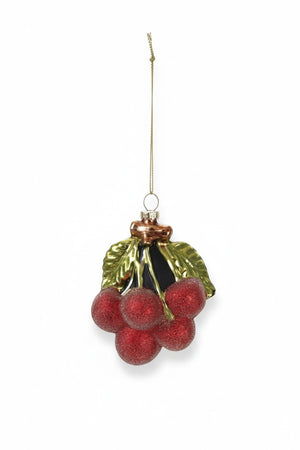 A GLASS CHERRY CLUSTER ORNAMENT WITH GLITTER and a green leaf hangs over a gift wrapped in cherry-patterned paper.