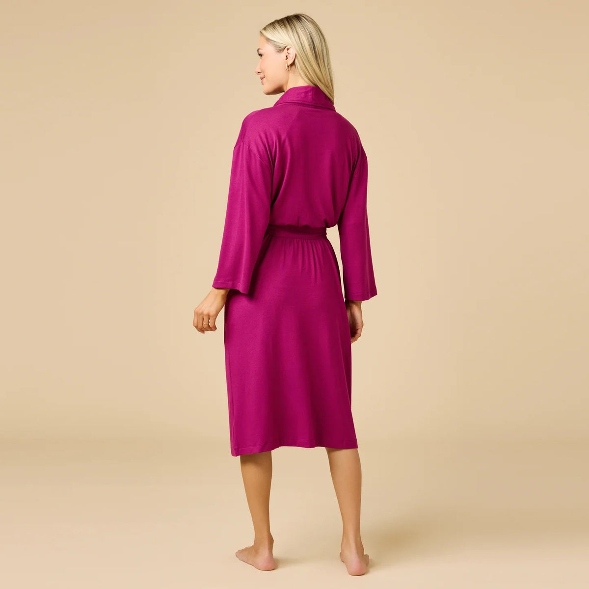 A woman wears a SOFTIES - DREAM SHAWL COLLAR ROBE in pink and white stripes, featuring a shawl collar, a tie waist, and three-quarter length sleeves.