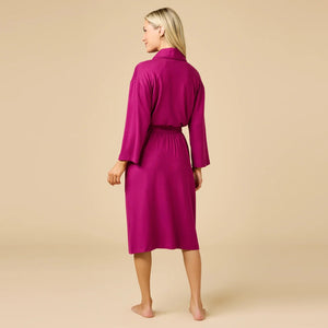 A woman wears a SOFTIES - DREAM SHAWL COLLAR ROBE in pink and white stripes, featuring a shawl collar, a tie waist, and three-quarter length sleeves.