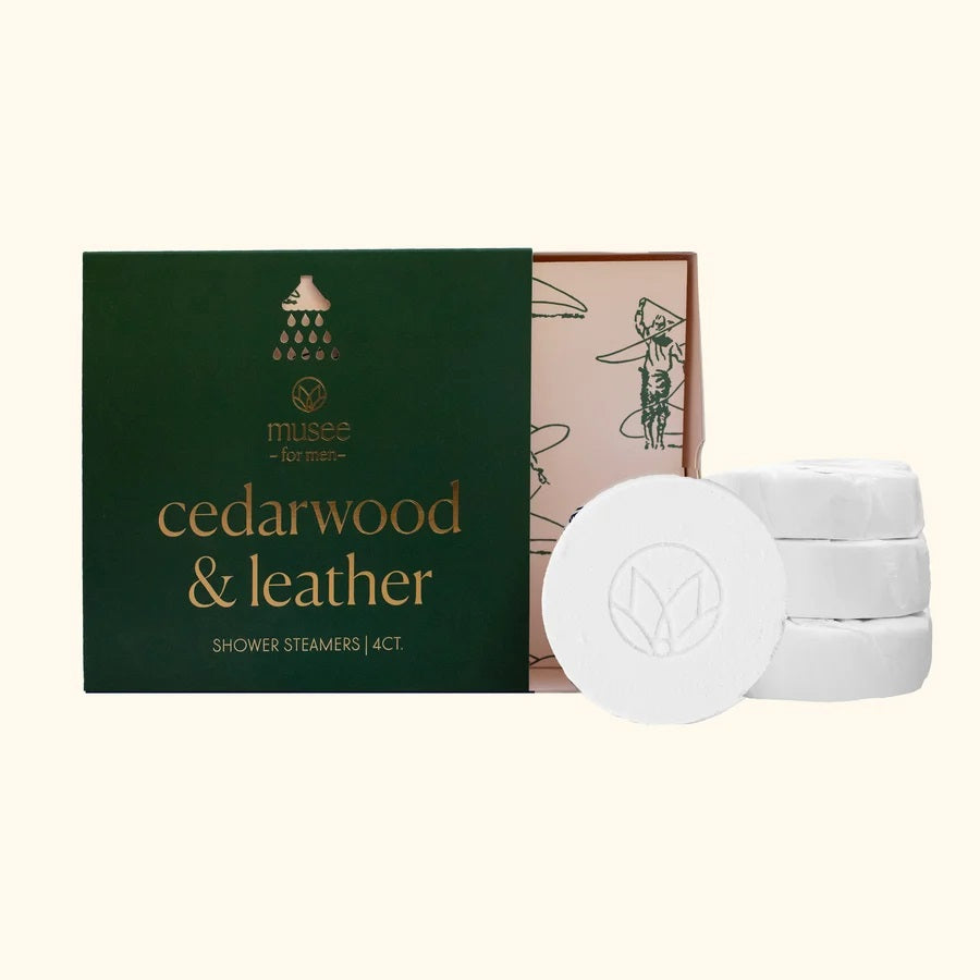 Pink graphic featuring the MUSEE - CEDARWOOD & LEATHER SHOWER STEAMERS in elegant flower-shaped packaging. Infused with a calming blend of cedarwood essential oil, this shower steamer by MUSEE elevates your daily routine into a spa-like retreat. Instructions: Turn on the shower for steam, place the steamer on the floor, let water drizzle over it, relax, reset, and enjoy.