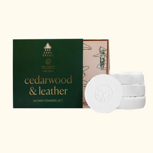 Pink graphic featuring the MUSEE - CEDARWOOD & LEATHER SHOWER STEAMERS in elegant flower-shaped packaging. Infused with a calming blend of cedarwood essential oil, this shower steamer by MUSEE elevates your daily routine into a spa-like retreat. Instructions: Turn on the shower for steam, place the steamer on the floor, let water drizzle over it, relax, reset, and enjoy.