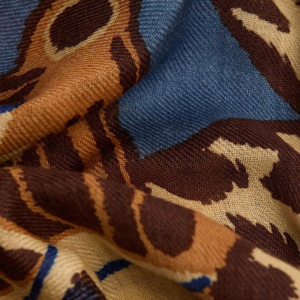 A woman with short blond hair and a beige sweater wears the INOUI EDITIONS PAPILLON (BUTTERFLIES) wool square scarf in duck blue, featuring colorful patterns, standing against a plain white background.