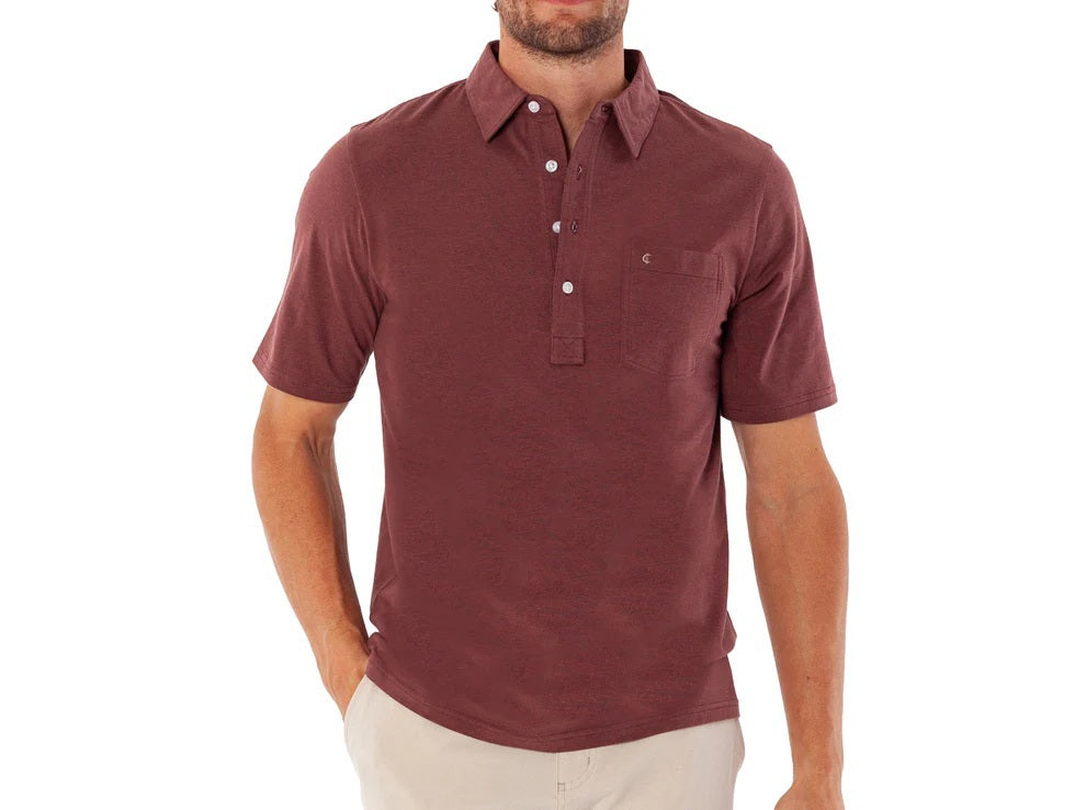 A man wearing the CRIQUET Top-Shelf Players Shirt in Mudslide Microstripe and beige pants stands with one hand in his pocket, smiling and looking to his left.