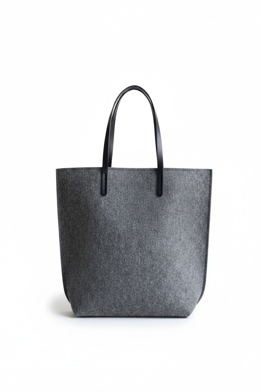 A person in a beige trench coat holds the WOOLBERRY WOOL FELT LONG TOTE BAG with black handles, standing against a plain, light-colored background.