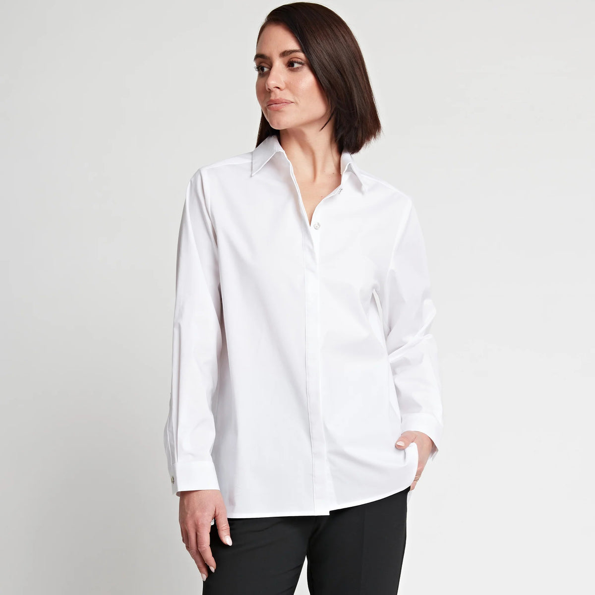 A person with medium-length dark hair wearing the HINSON WU SARA Long Sleeve Pleated Back Shirt, featuring a shirt collar and long sleeves, paired with black pants, stands against a plain white background. They have one hand in their pocket and are gazing slightly to the side, giving a relaxed and contemplative expression.
