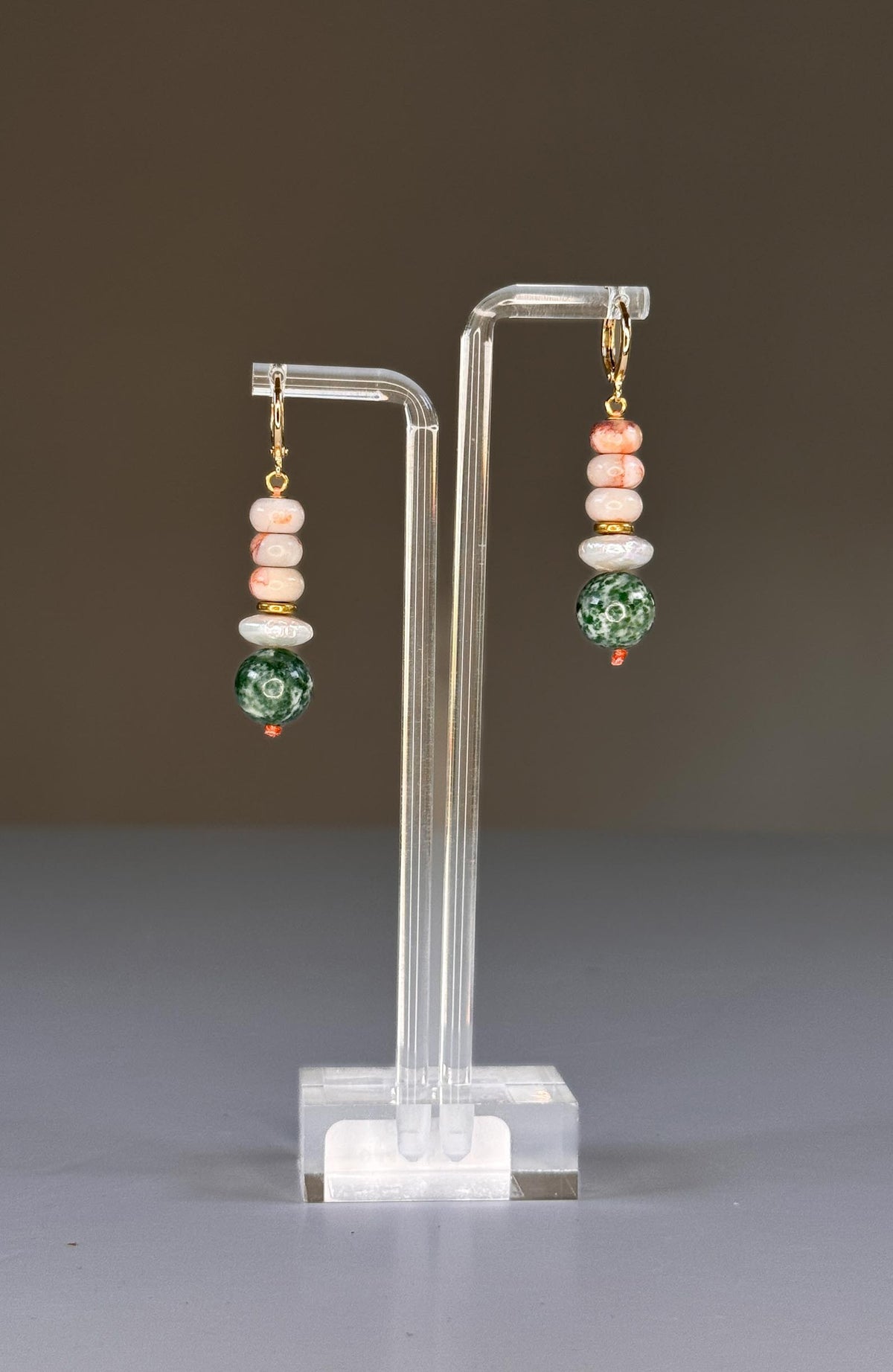 The SELENA EARRINGS by SANDRINE FRANCE STUDIO are gold hoops with stacked beige and brown marbled beads, a white pearl-like accent, gold spacer, and a large green-and-white Tree Agate bead, displayed on a plain background.