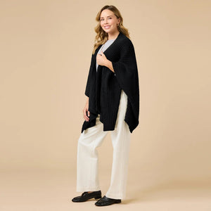 A woman wearing a black SOFTIES - SOLID RIB MARSHMALLOW SHAWL over a grey top and white trousers.