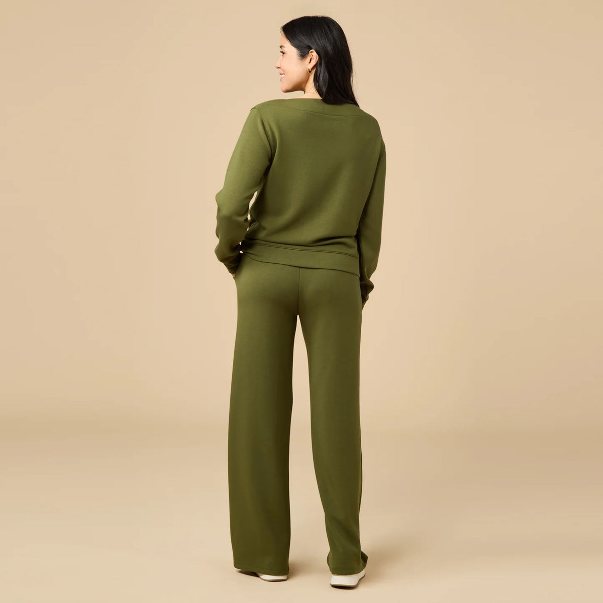 A woman wears a SOFTIES - DREAMTECH BOAT NECK WITH PINTUCK PANT SET in olive green, featuring a long-sleeve boat neck top and matching wide-leg pintuck pants.