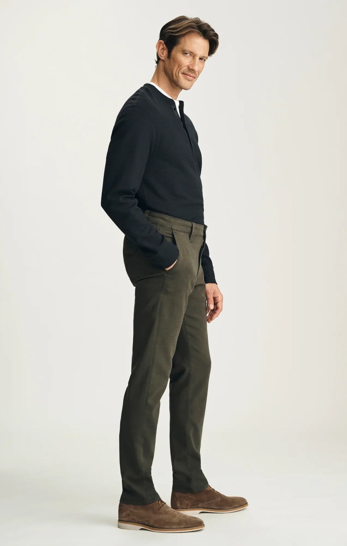 A person stands with their back to the camera against a neutral background, wearing the 34 HERITAGE - VERONA Straight Leg Chino Pant in Jasper High Flyer paired with a black long-sleeve shirt and brown suede shoes.