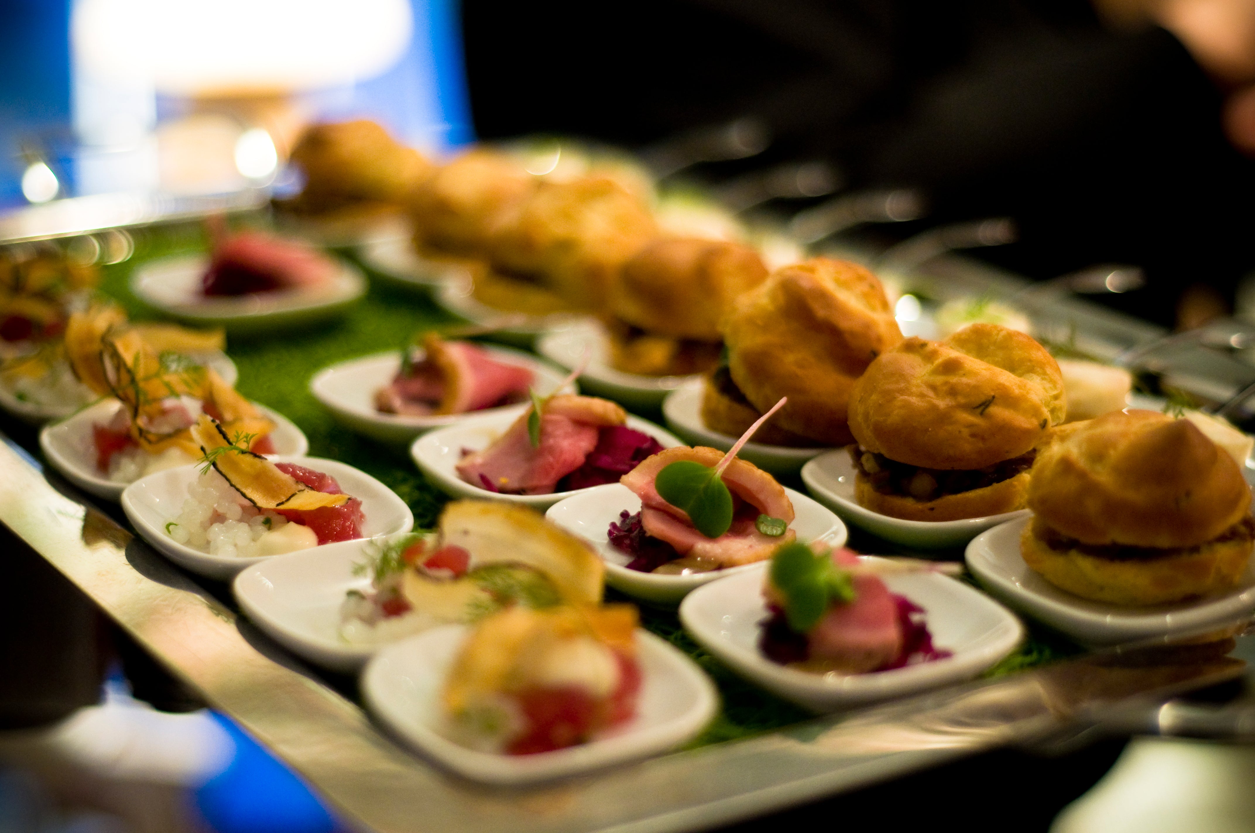 A tray of assorted gourmet appetizers on small white plates, including mini sandwiches, pastries, and bite-sized portions of meat and vegetables, arranged neatly for a catered event.