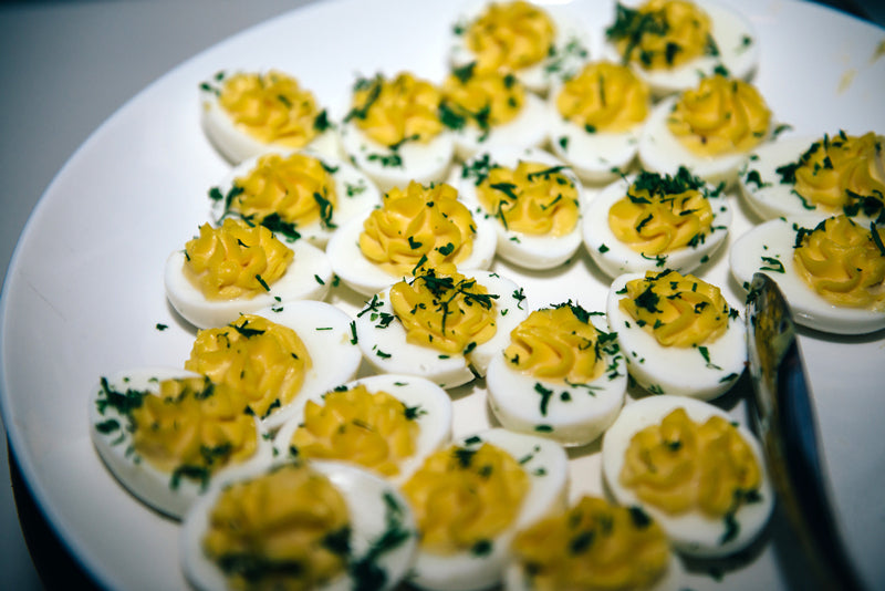 A white plate filled with several deviled eggs, topped with a yellow yolk mixture and garnished with chopped green herbs, is shown close-up.