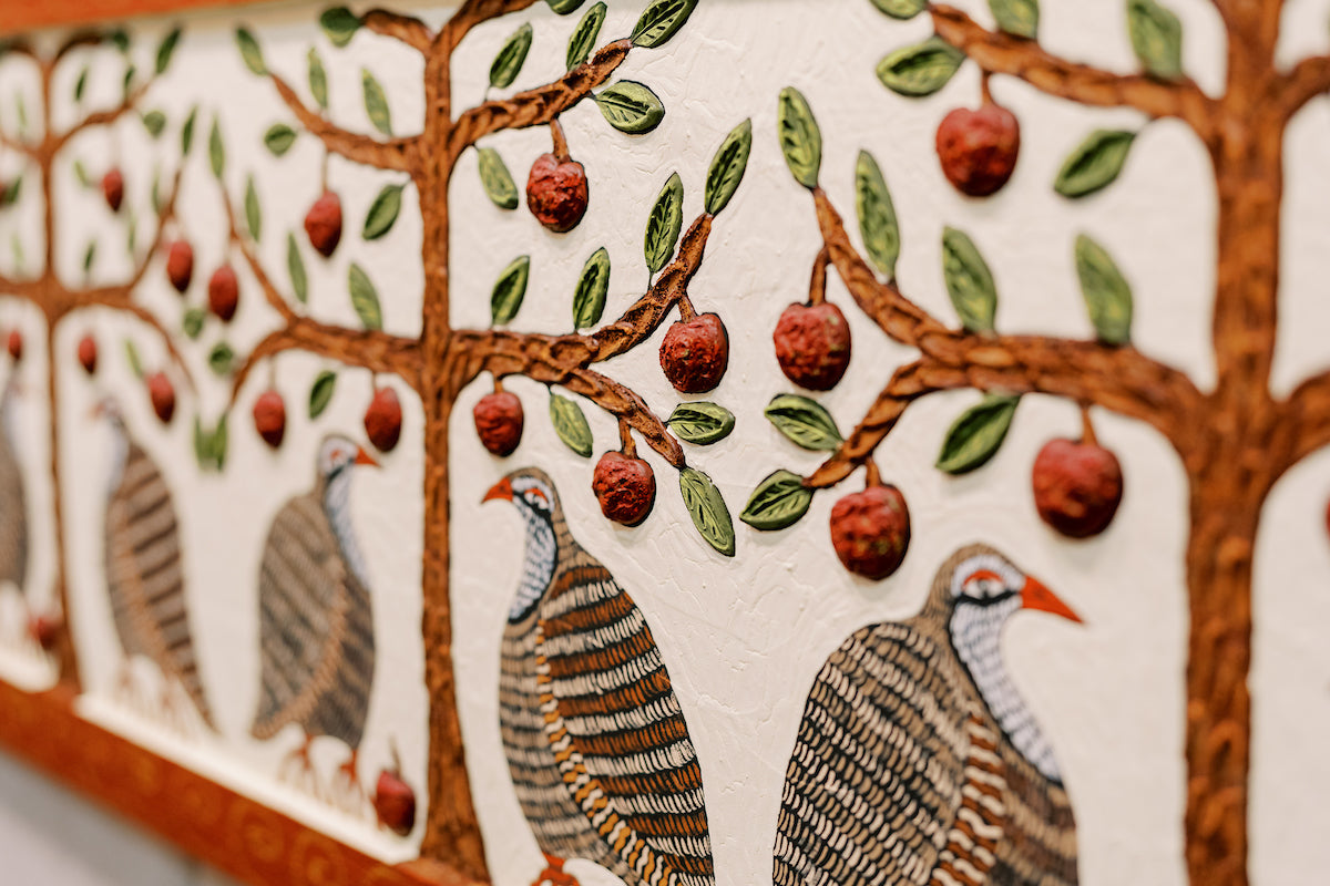 A textured painting shows several guinea fowl with red beaks standing under brown trees with green leaves and red fruit, against a cream-colored background. The artwork features bold lines and raised details.