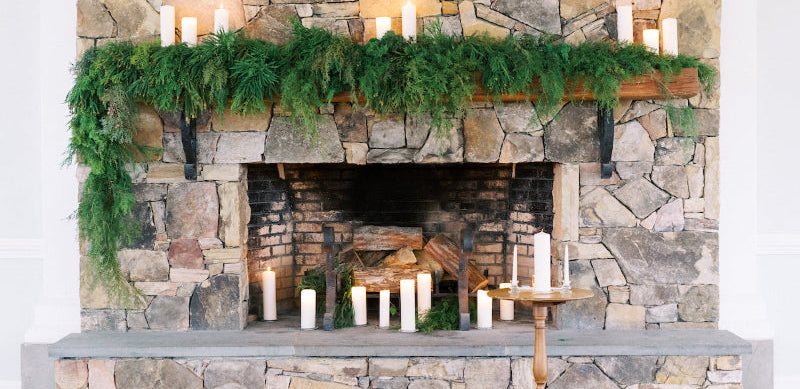 Stone fireplace with greenery and candles against a stone wall.