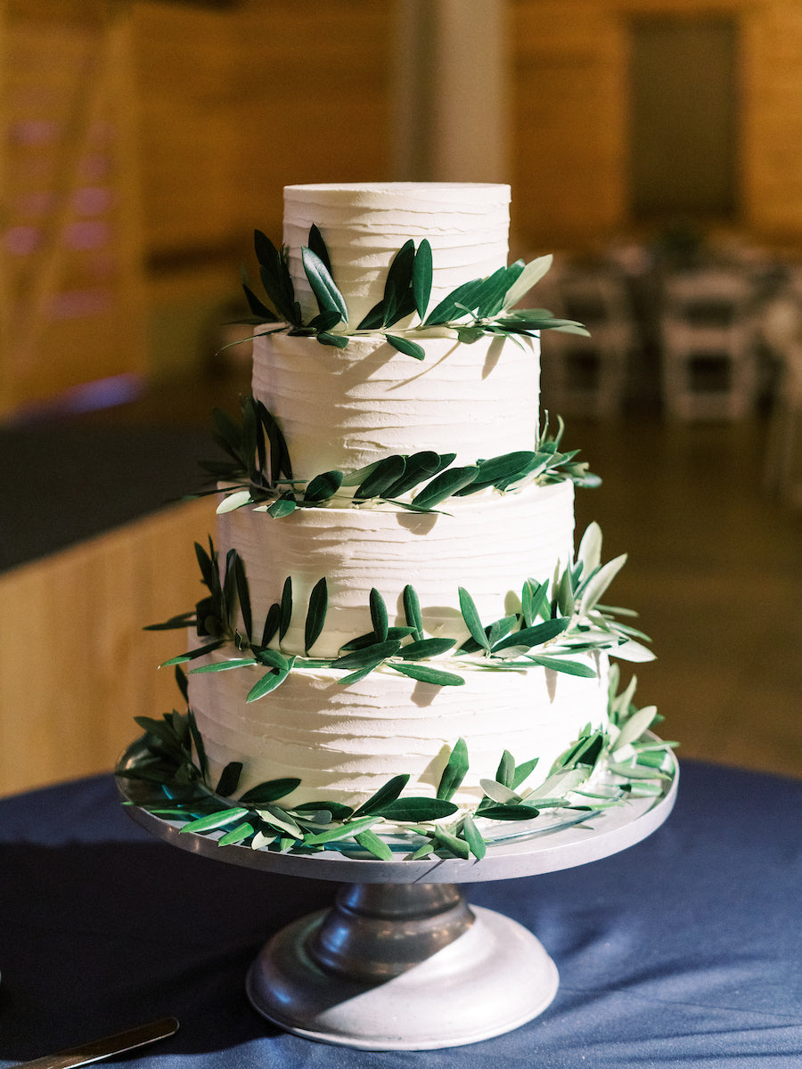 Three-tiered white cake with green leaf decorations on a stand.