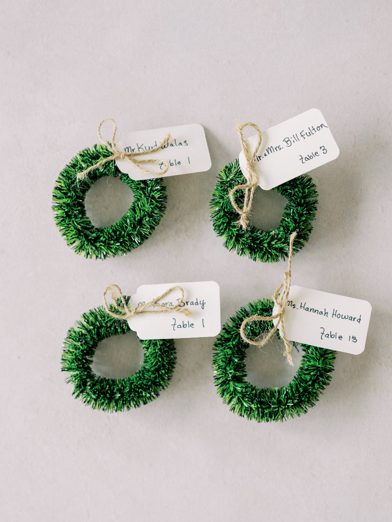 Four small green wreath place cards on a light gray background