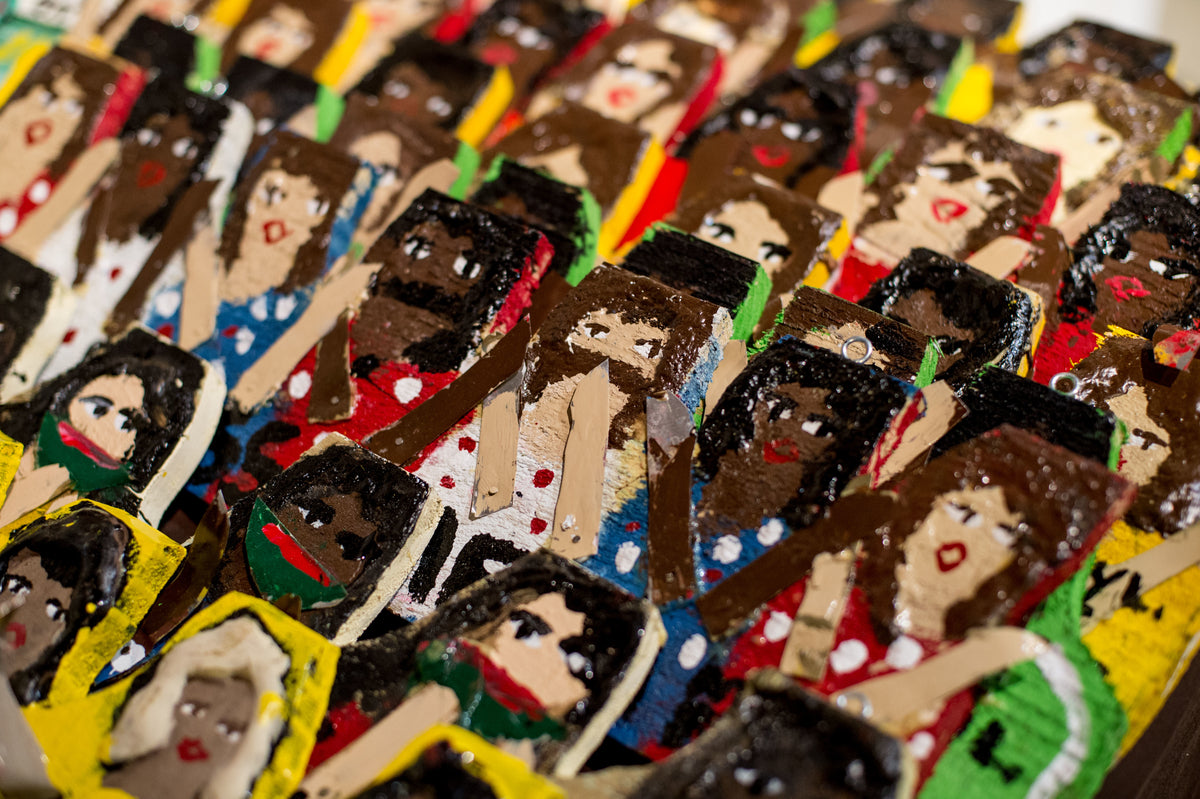 Rows of hand-painted wooden figurines with various skin tones, brown and black hair, and red lips, all wearing colorful polka-dot clothing and standing closely together.