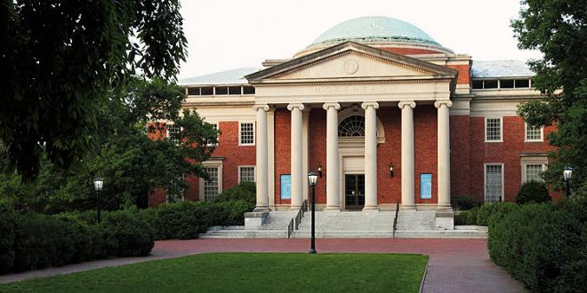 A red-brick building with white columns, large steps, and a domed roof, surrounded by trees and greenery, with a pathway leading to the entrance.