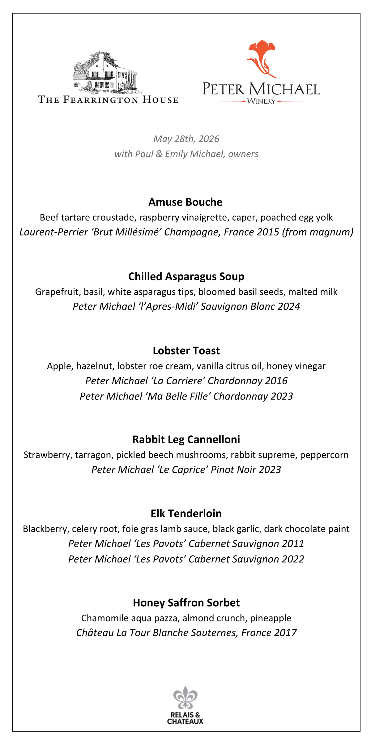 A man in a straw hat and a woman in a denim jacket smile together outdoors by a wooden bench with a stag carving—an inviting scene evoking the Peter Michael Wine Dinner by FEARRINGTON VILLAGE, surrounded by tall trees and greenery.