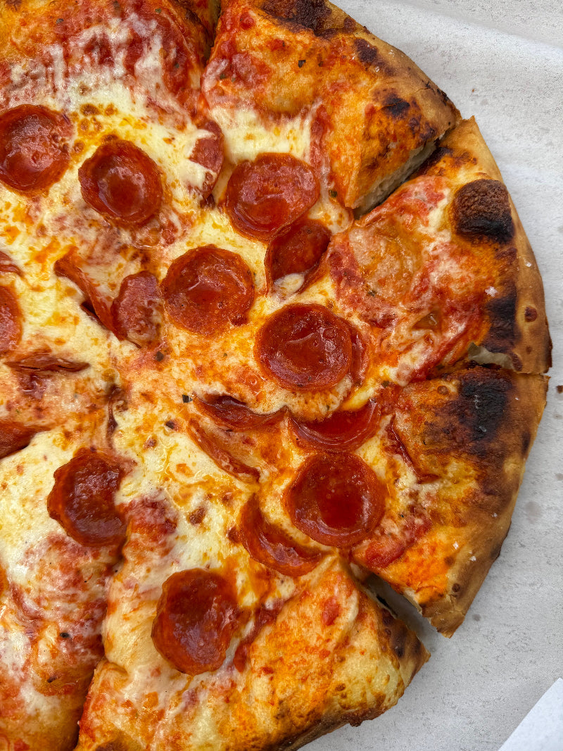 A close-up of a pepperoni pizza with melted cheese and crispy, slightly charred crust, cut into slices.