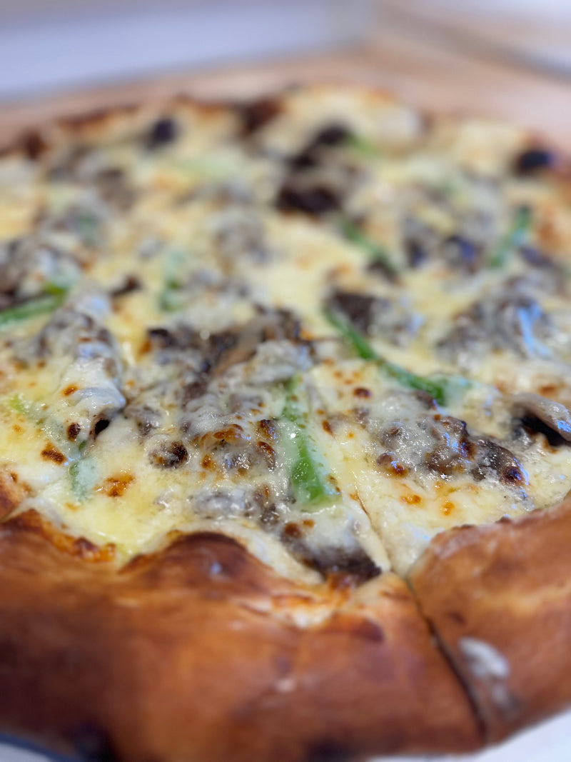 Close-up of a freshly baked pizza with melted cheese, green bell peppers, mushrooms, and browned edges on a thick crust.
