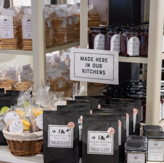 A display of local products including jars of jam, packaged cookies, and bags of coffee, with a sign reading 