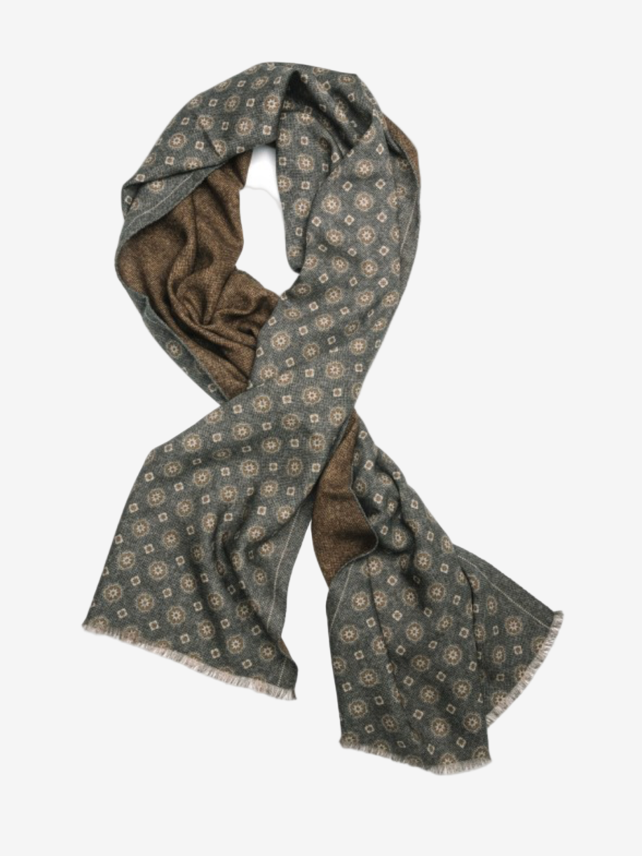 A long scarf with a blue and brown geometric pattern and frayed edges, laid out in a loose loop on a white background.