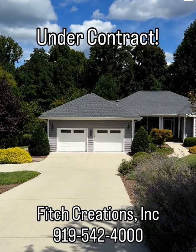 A suburban house with a gray roof and white garage doors, surrounded by green trees and bushes. Text reads “Under Contract! Fitch Creations, Inc 919-542-4000.”.