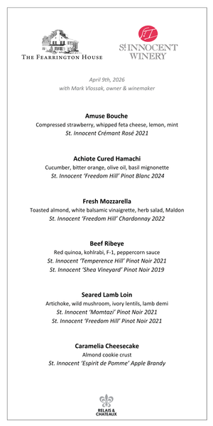 An older man with gray hair and glasses, in a red shirt and gray vest, smiles as he holds a small plant before shelves of greenery, capturing the inviting charm of a FEARRINGTON VILLAGE St. Innocent Wine Dinner.