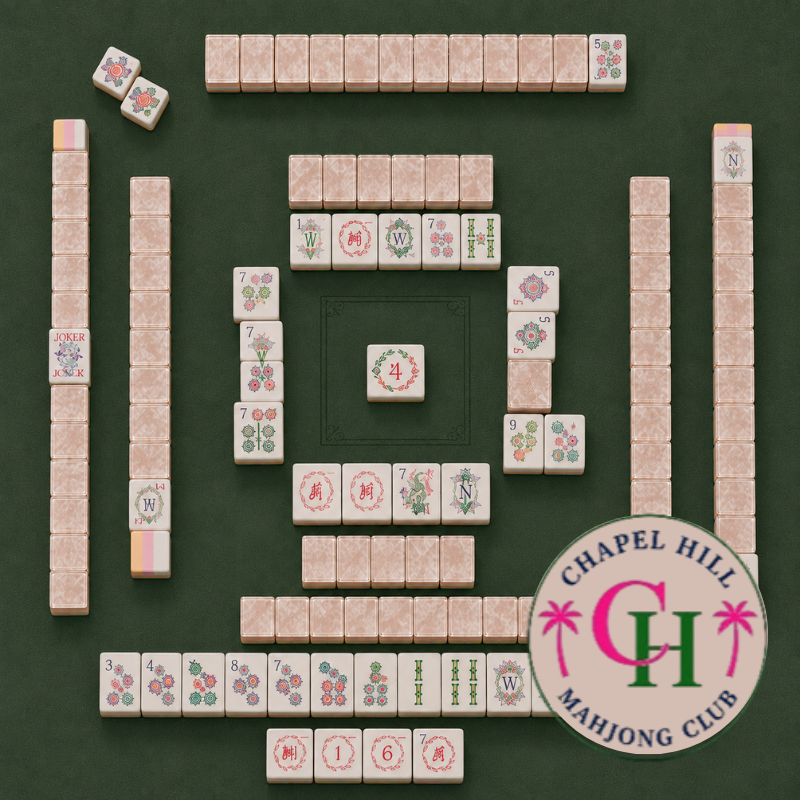 Mahjong tiles are arranged on a green table featuring the “FEARRINGTON VILLAGE” logo for MAHJONG NIGHT AT FEARRINGTON in the lower right corner. Various suits and honor tiles are neatly organized in rows and squares, reflecting the popular style of play enjoyed by participants from both Fearrington Village and Chapel Hill.
