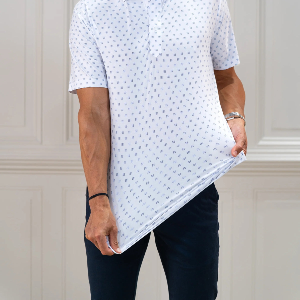 The COLLARS AND CO FEATHERWEIGHT FLEX POLO IN ORACLE WHITE features white fabric with a repeating pattern of small blue 3x3 dot squares. Slightly creased at the center, its 6-way stretch design ensures all-day comfort.