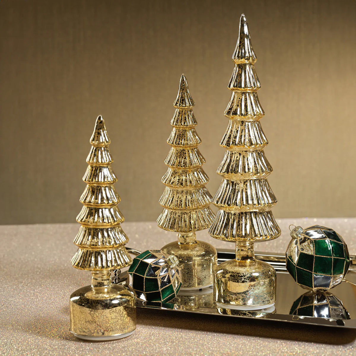 The ZODAX ALPINE ROTATING LED TREE IN ANTIQUE GOLD - LARGE is a decorative Christmas tree with tiered branches on a round base, featuring a glass LED light that brings a warm festive glow.