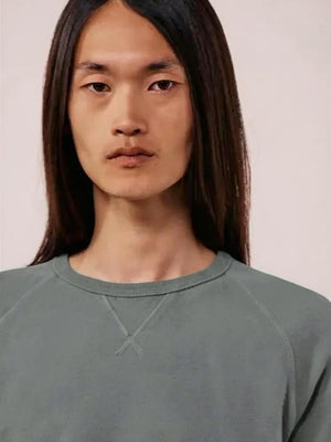 A close-up view of a person wearing the HARTFORD light fleece sweatshirt in charcoal, made in Portugal, featuring a distinctive X-shaped decorative stitch detail at the base of the collar.